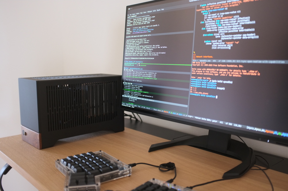 Office desk with a workstation, a keyboard and a monitor displaying the Emacs text editor.